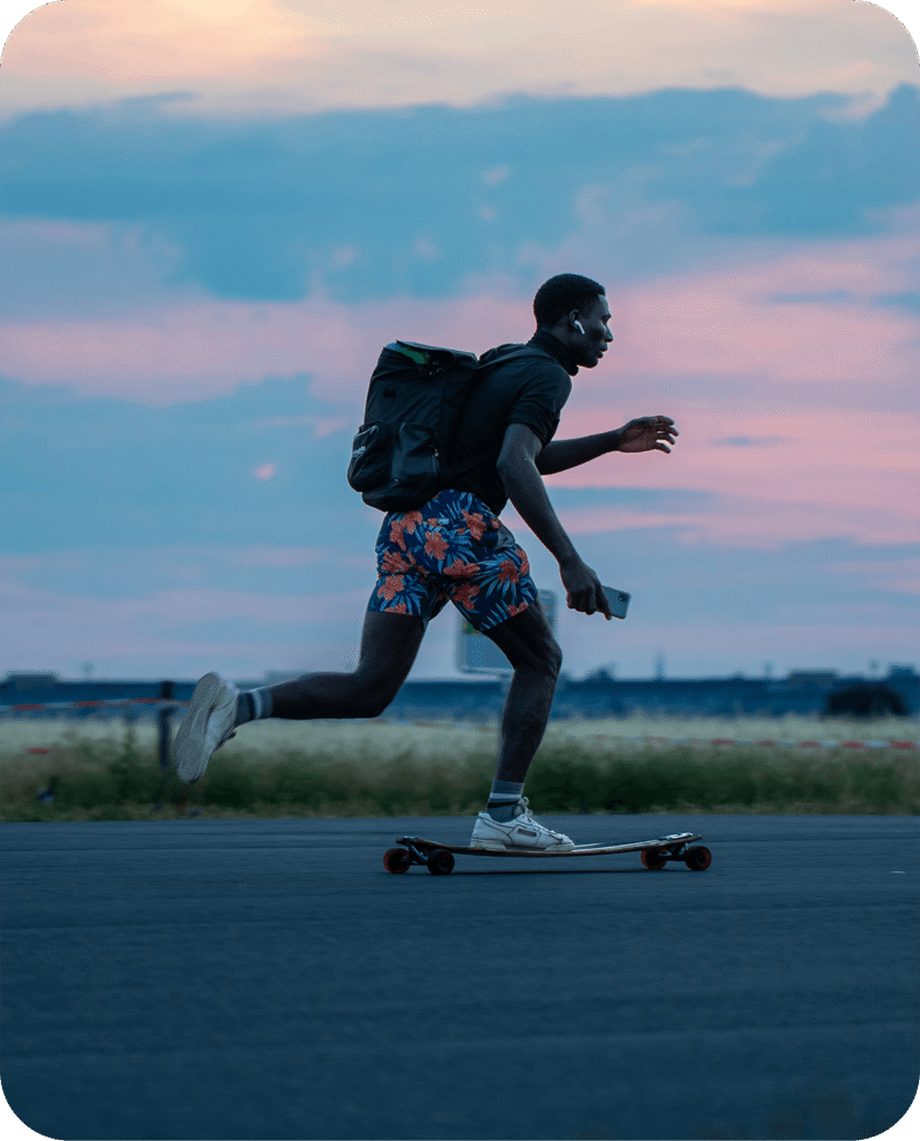 An energetic lifestyle photo of a man longboarding during golden hour sunset with a backpack and earbuds.