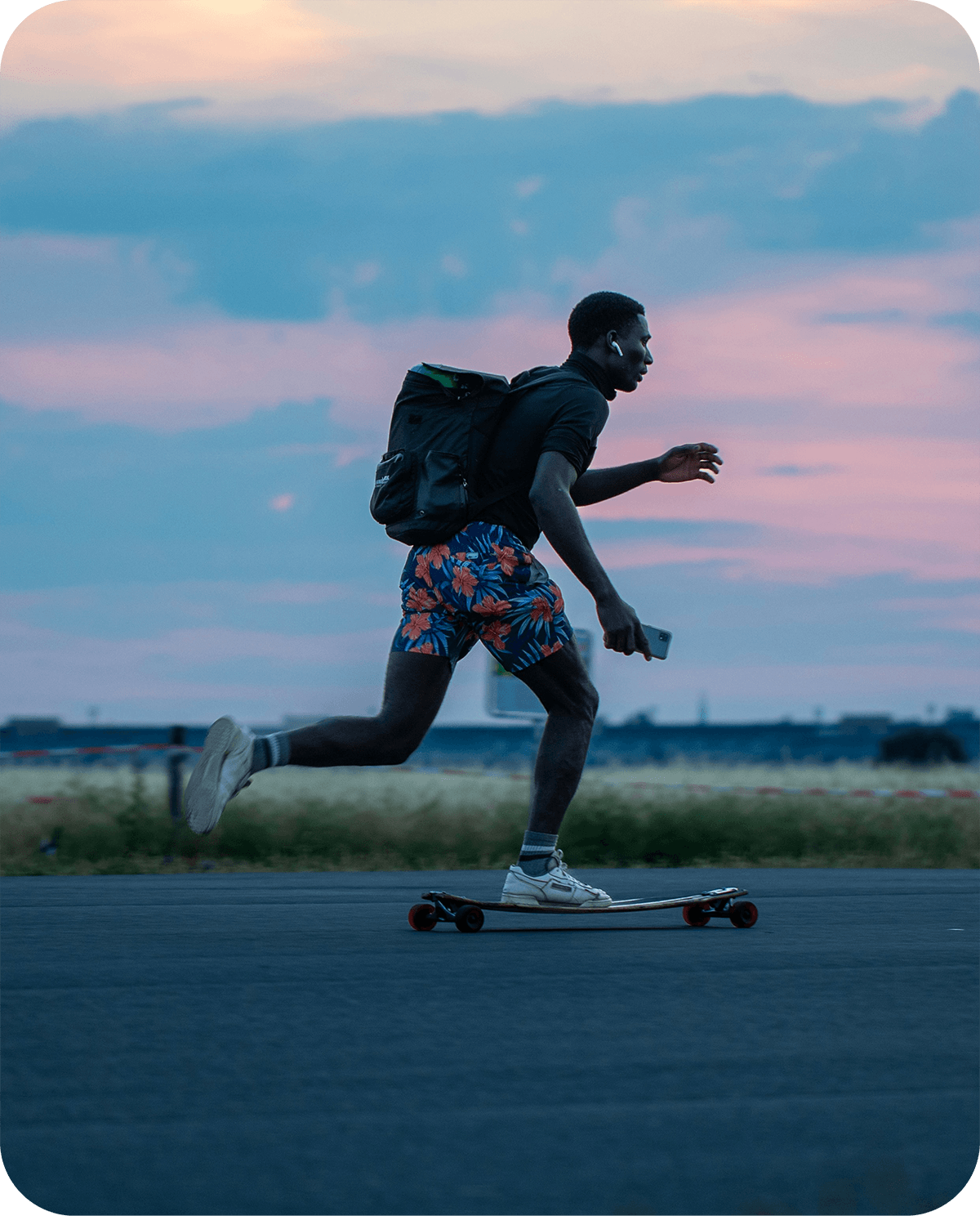 An energetic lifestyle photo of a man longboarding during golden hour sunset with a backpack and earbuds.